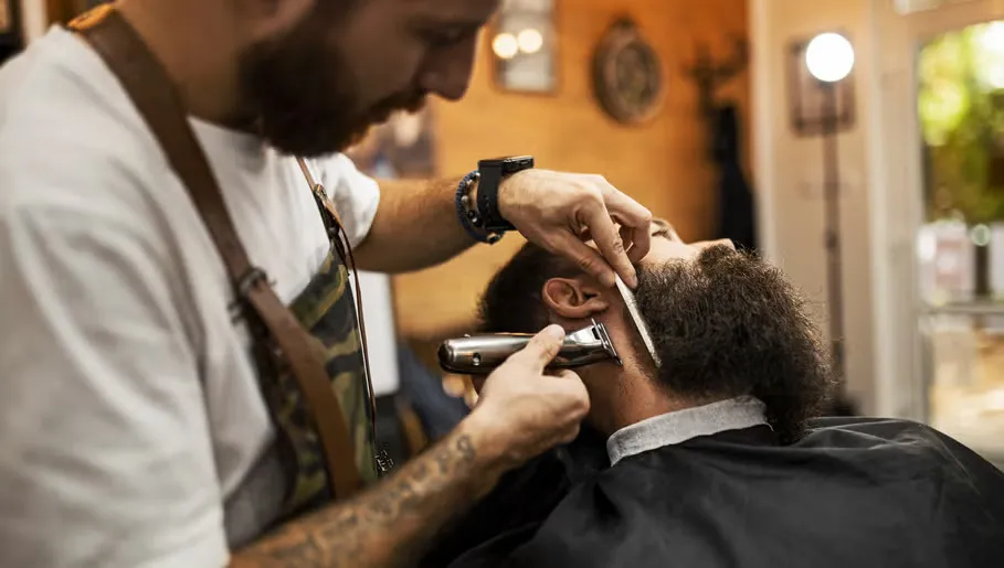 Barbeiro a aparar a barba de um cliente com máquina e pente