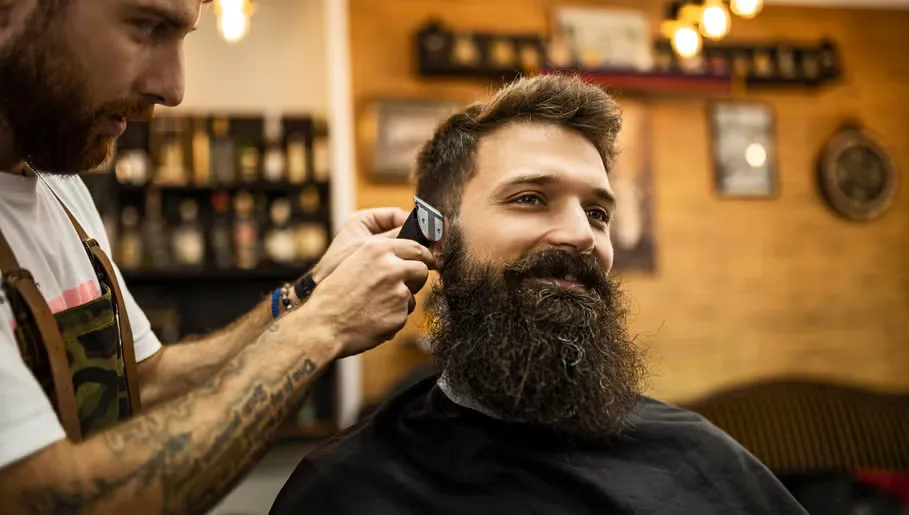 Cliente de barba comprida a sorrir enquanto o barbeiro lhe corta o cabelo à máquina